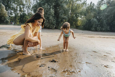 Mother and daughter discovering crab at beach - MFF06274