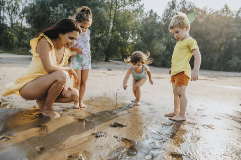 Mature woman and children discovering crab at beach stock photo