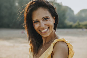 Lächelnde Frau am Strand stehend an einem sonnigen Tag - MFF06280