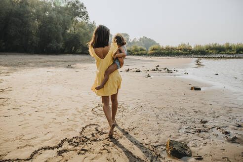 Mother carrying daughter while walking on sand at beach - MFF06282