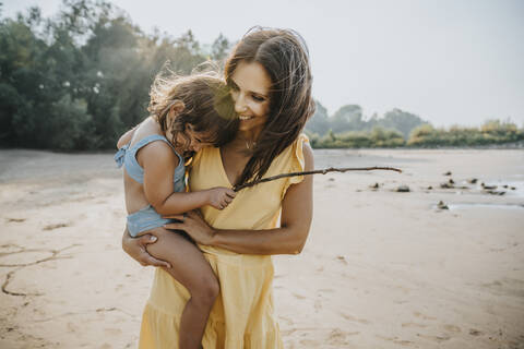 Happy mother holding daughter in arms at beach stock photo