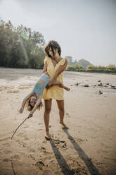 Mother whirling daughter while standing at beach - MFF06285