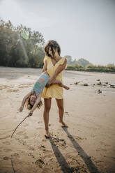 Mutter wirbelt Tochter am Strand stehend - MFF06285