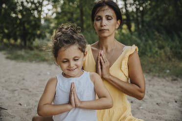 Mother and daughter meditating at beach - MFF06291