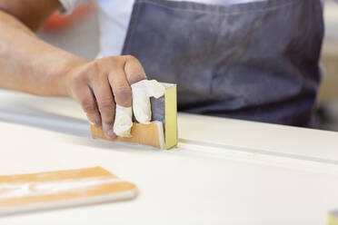 Carpenter hand sanding wood while standing at workshop - EIF00236