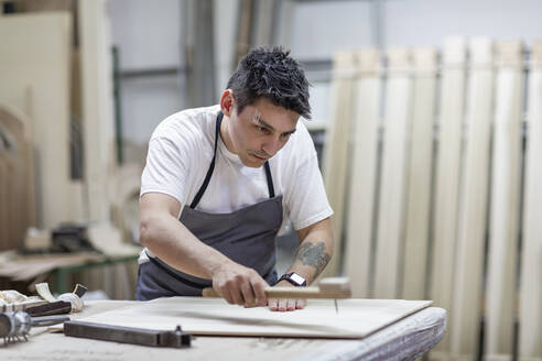 Künstlerin, die in der Werkstatt stehend dem Holz mit traditionellen Methoden eine Form gibt - EIF00260