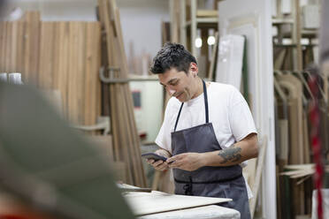 Männlicher Künstler, der ein Mobiltelefon benutzt, während er in einer Werkstatt steht - EIF00262