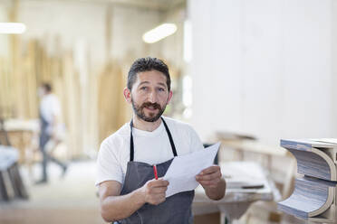 Lächelnder Mann mit Papier in der Hand in einer Werkstatt stehend - EIF00267