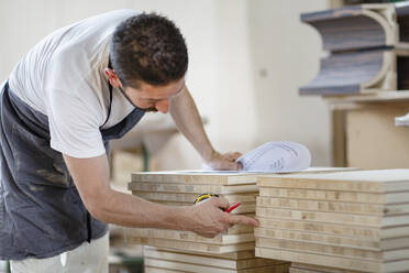 Mann zählt Holzbretter bei der Arbeit in der Werkstatt - EIF00268