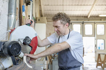 Ein Mann bedient eine elektrische Säge, während er in einer Werkstatt steht - EIF00269