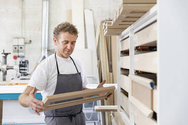 Carpenter holding frame while standing at workshop - EIF00272