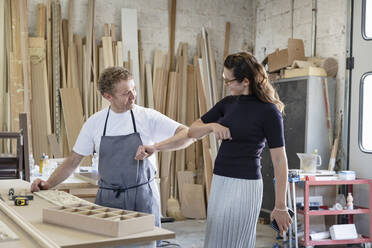 Lächelnder Mann und lächelnde Frau stoßen sich mit den Ellbogen an, während sie in der Werkstatt stehen - EIF00280