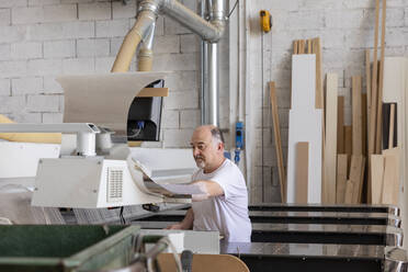 Ein älterer Mann bedient eine Holzschneidemaschine, während er in einer Fabrik sitzt - EIF00294