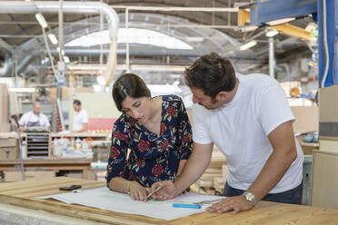 Projektleiter und Architekt besprechen den Plan mit einem Mitarbeiter, der im Hintergrund in einer Fabrik arbeitet - EIF00314