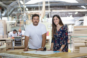 Projektleiter und Architekt diskutieren im Stehen mit einem Mitarbeiter, der im Hintergrund in einer Fabrik arbeitet - EIF00315