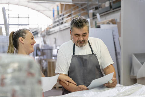 Smiling coworker and secretary reading shipment paper while standing at factory stock photo