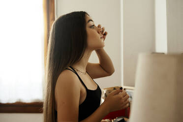 Long hair teenage girl applying make up while standing at home - ERRF04559