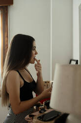 Teenager girl applying lipstick while standing at home - ERRF04560