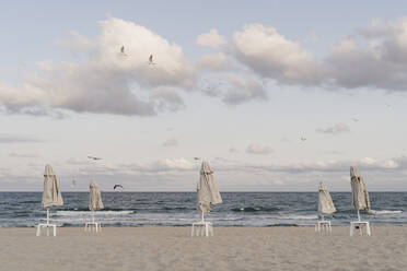 Clouds over beach umbrellas standing on empty beach at dusk - AFVF07310