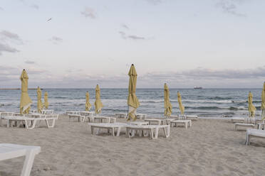Sonnenschirme und Liegestühle am leeren Strand in der Abenddämmerung - AFVF07311