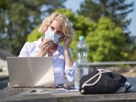 Frau mit Maske sitzt mit Laptop im Hinterhof - LAF02482