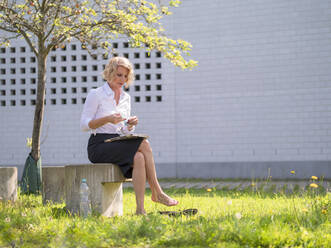 Geschäftsfrau mit Gesichtsmaske, die auf einer Bank im Hinterhof sitzt - LAF02483