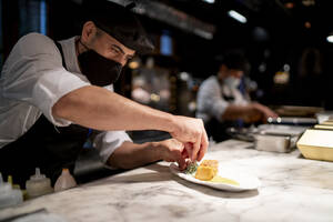 Chef garnishing pudding while standing in restaurant kitchen - OCMF01739