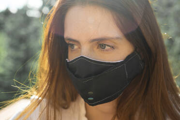 Close-up young woman wearing protective face mask looking away - AFVF07314
