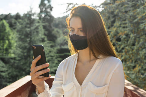 Junge Frau trägt Schutzmaske, während sie ein Selfie mit ihrem Smartphone macht, lizenzfreies Stockfoto