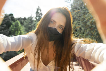 Young woman wearing protective face mask taking selfie on sunny day - AFVF07316