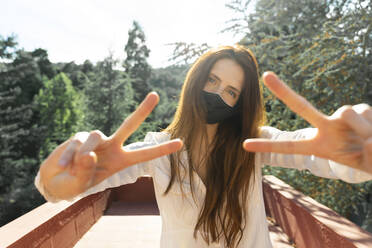 Junge Frau mit Gesichtsschutzmaske, die auf einem Balkon stehend eine Handbewegung macht - AFVF07318