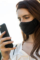 Young woman text messaging on smart phone wearing protective face mask - AFVF07322