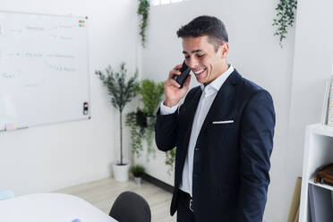Smiling businessman talking on mobile phone while working at creative office - GIOF09068