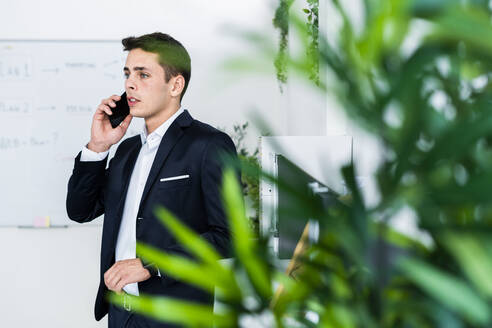 Gut aussehender junger Mann, der am Telefon spricht, während er an einem kreativen Arbeitsplatz steht - GIOF09079