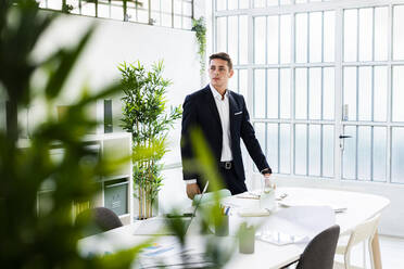 Handsome businessman looking away while standing at desk in creative office - GIOF09083