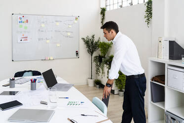 Male professional looking at laptop on desk while standing in creative office - GIOF09103