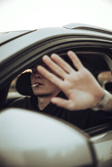 Junger Mann zeigt Stopp-Geste beim Rauchen einer Zigarette im Auto - ACPF00823