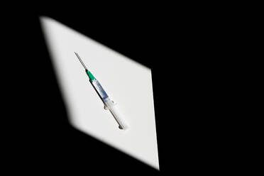 From above sterile syringe with drop of remedy on needle on blurred black background - ADSF16599