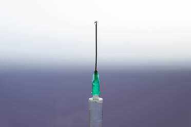 Closeup of sterile syringe with drop of remedy on needle on blurred gradient background - ADSF16600