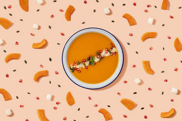 Studio shot of bowl of pumpkin soup surrounded by pumpkin seeds, pomegranate seeds and pieces of cheese and pumpkin - GEMF04212