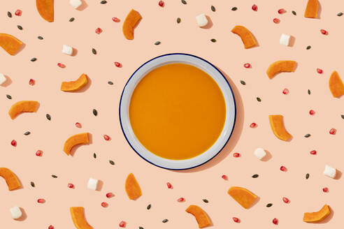 Studioaufnahme einer Schüssel mit Kürbissuppe, umgeben von Kürbiskernen, Granatapfelkernen und Stücken von Käse und Kürbis - GEMF04213
