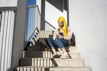Junge Frau benutzt ihr Smartphone, während sie auf einer Treppe sitzt - VPIF03110