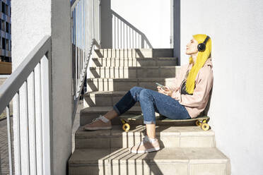 Young woman listening music through headphone sitting on staircase - VPIF03111