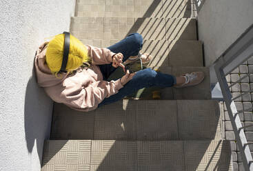 Woman text messaging and listening music while sitting on steps during sunny day - VPIF03113