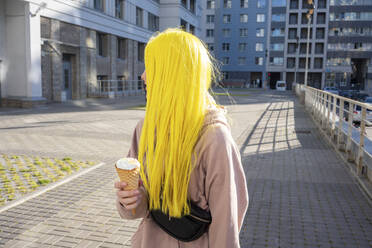 Junge Frau schaut weg, während sie auf der Straße stehend eine Eistüte isst - VPIF03118