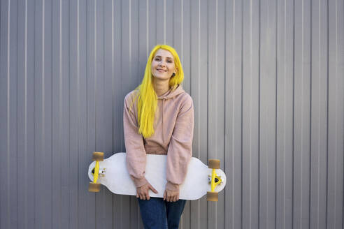 Junge Frau mit Skateboard an einer Metallwand stehend - VPIF03126