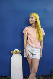 Junge Frau mit Skateboard steht gegen blaue Wand - VPIF03135