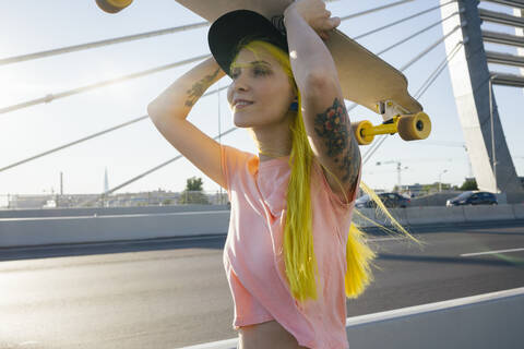 Junge Frau mit Skateboard auf dem Kopf an einem sonnigen Tag, lizenzfreies Stockfoto