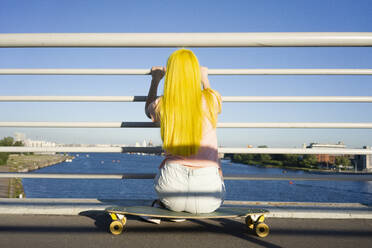 Langhaarige Frau schaut auf das Meer, während sie auf einem Skateboard sitzt, während eines sonnigen Tages - VPIF03157