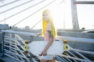 Frau mit Skateboard auf einer Brücke an einem sonnigen Tag - VPIF03161